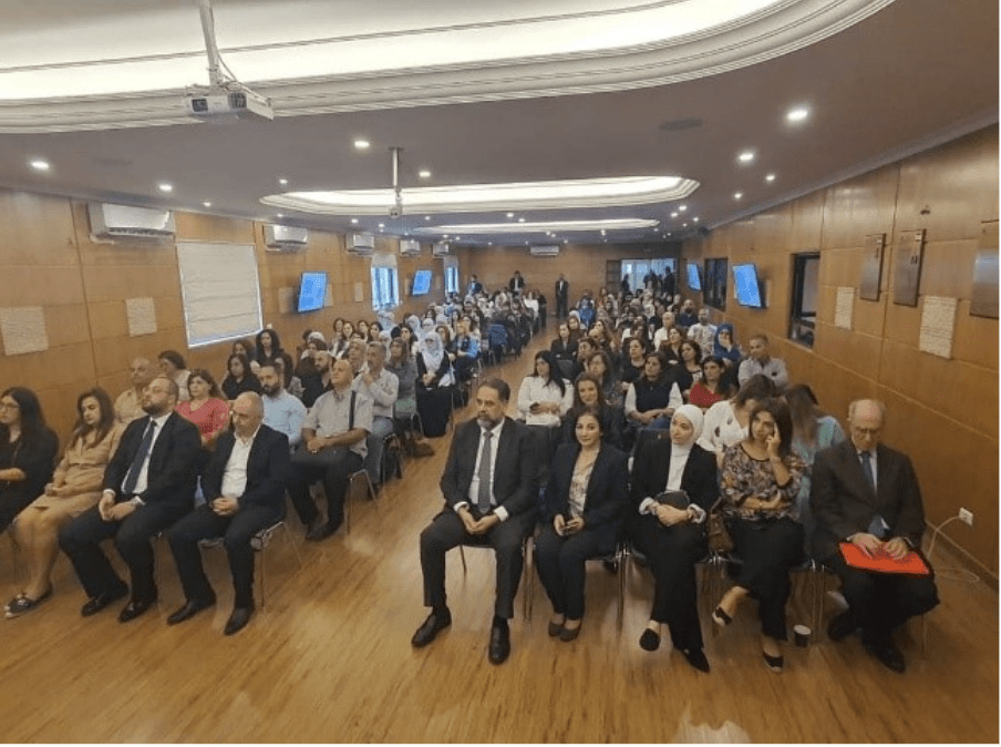 A diverse crowd seated in a spacious room listening to a presentation.